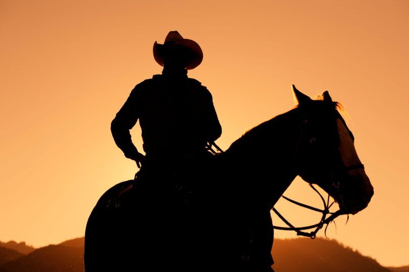 silhouette of cowboy wearing cowboy hat on horse