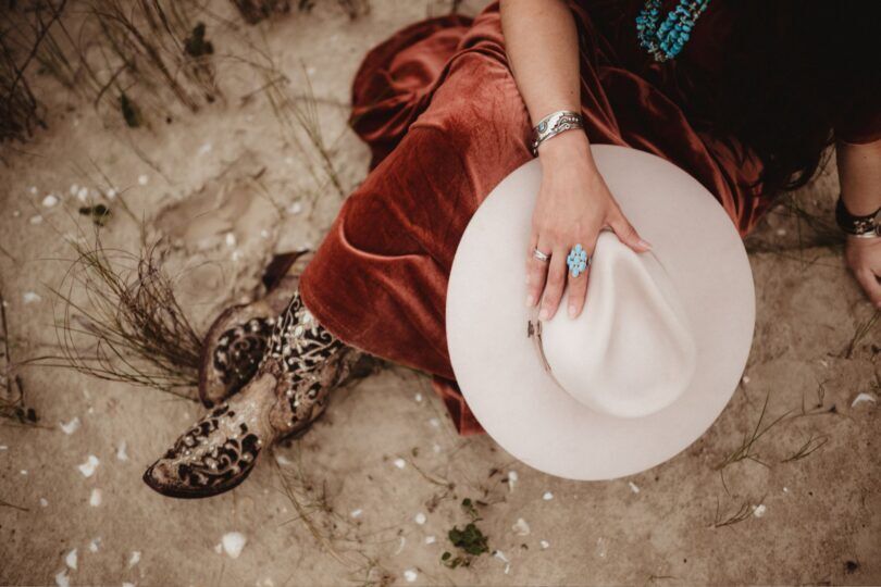 light colored cowboy hat held by woman wearing cowboy boots